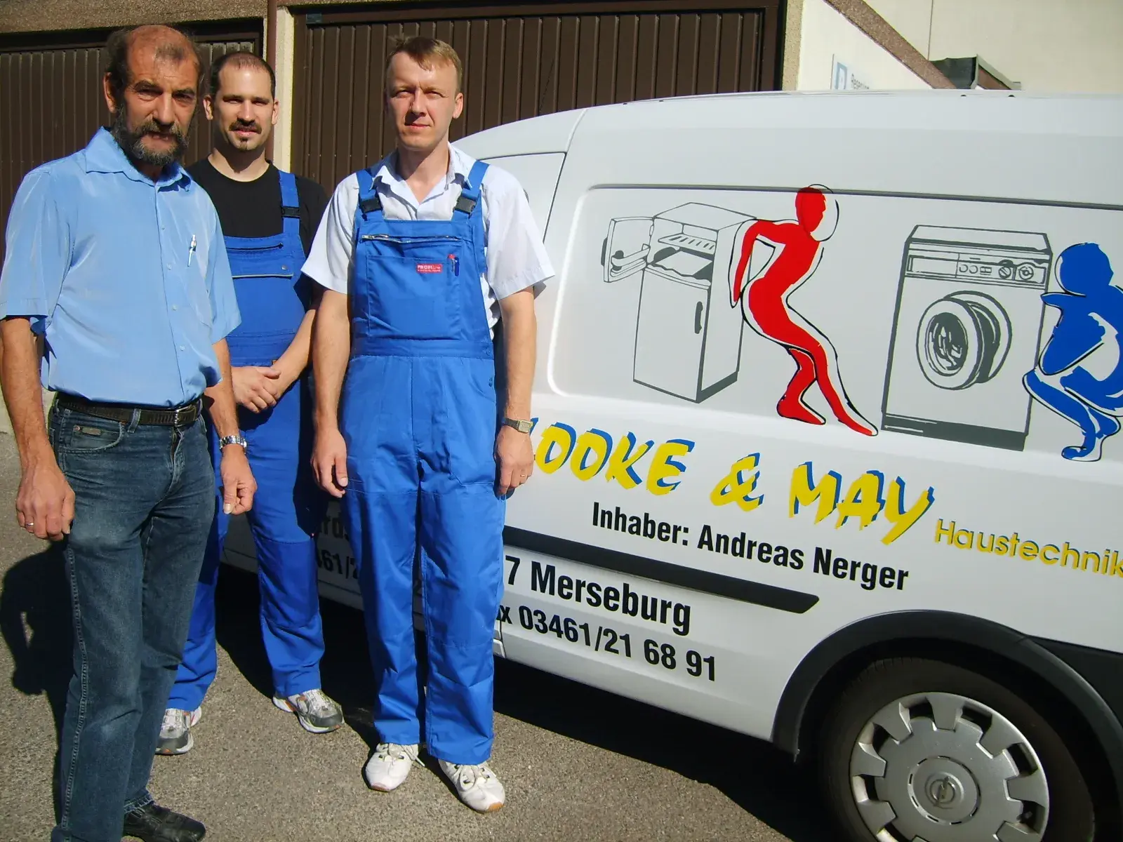 Drei Männer in Arbeitskleidung stehen neben einem Firmenfahrzeug mit Waschmaschinen-Werbung.